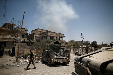 A member of the Iraqi rapid response forces walks past armoured vehicles as smoke rises in the background at the frontline in western Mosul, Iraq June 4, 2017. REUTERS/Alkis Konstantinidis