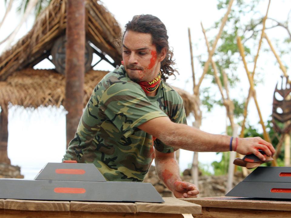 Ozzy Lusth wearing a green camo shirt and doing a puzzle on Survivor