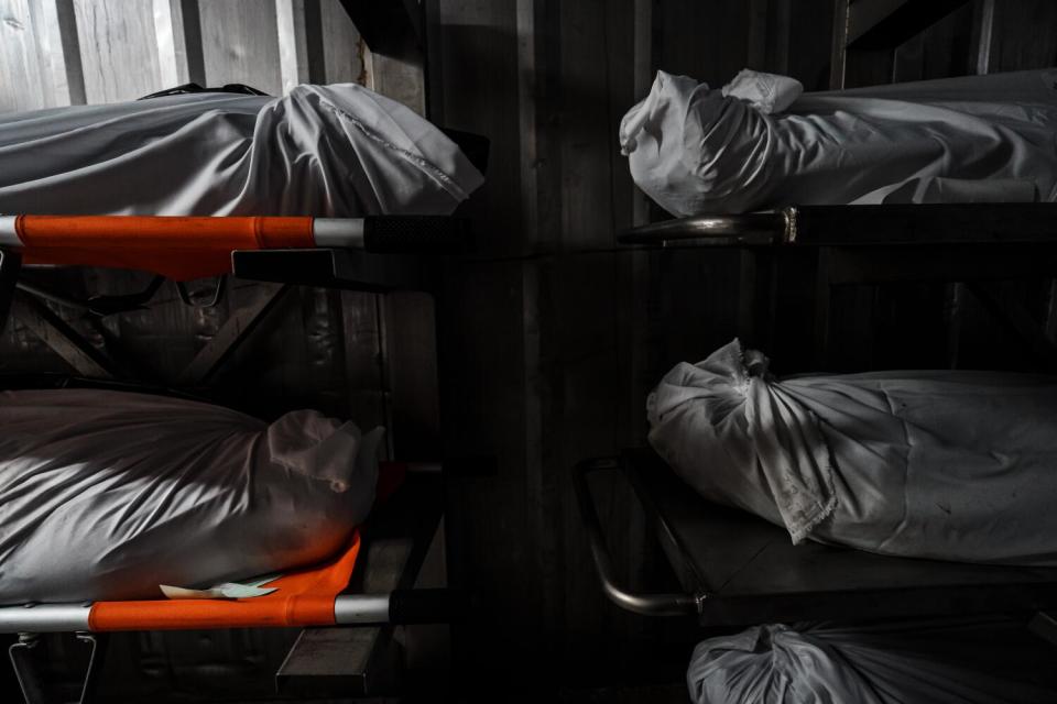 White body bags lie on stretchers in rows