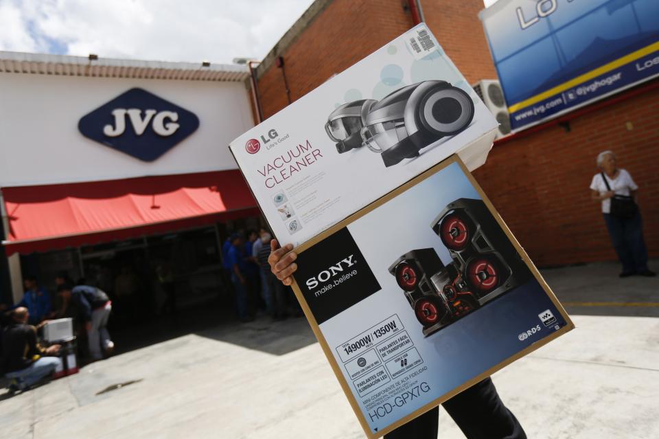 A shopper carries electronic goods outside an appliance store in Caracas