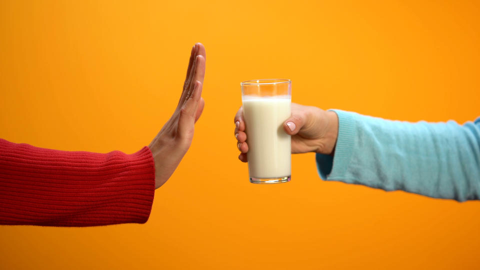 Female refusing to drink milk showing stop gesture on bright background, health. Here's what to know about milk allergies. (Getty)