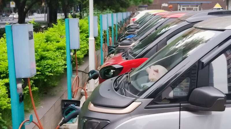 A row of electric vehicles all lined up and plugged in at charging stations.