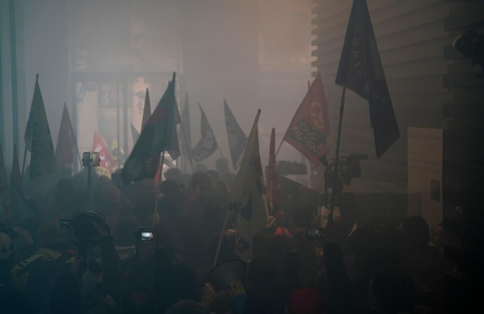 A group of protestors holding flags inside the smoke-filled interior of LVMH's headquarters.