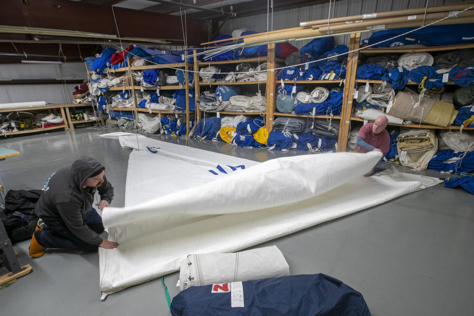 In this Monday, March 23, 2020 photo, Eric Baldwin, right, helps Alan Pratner fold a sail at North Sails in Freeport, Maine. The sail-maintenance business has converted part of its operation towards stitching masks instead of sails. (AP Photo/Robert F. Bukaty)