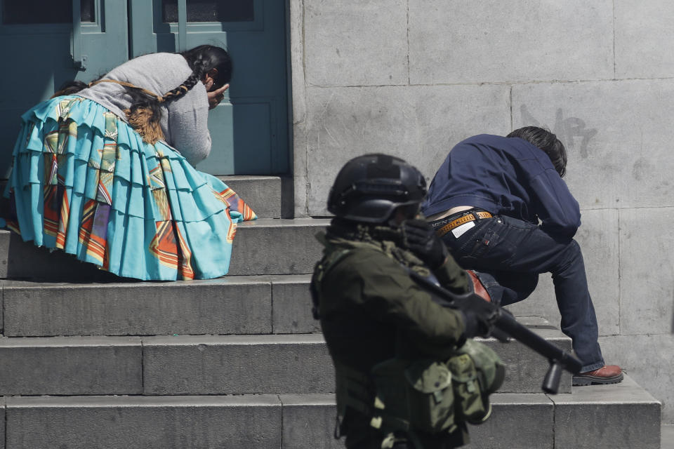 Pedestrians take cover from tear gas launched by security forces at anti-government demonstrators in La Paz, Bolivia, Thursday, Nov. 21, 2019. Backers of former President Evo Morales have taken to the streets asking for his return since he resigned on Nov. 10 under pressure from the military after weeks of protests against him over a disputed election he claim to have won. (AP Photo/Natacha Pisarenko)