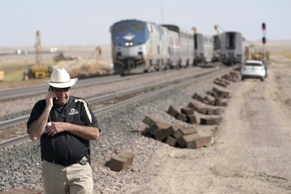 Jason Jarrett, of the Gallatin County (Mont.) Sheriff's Office, talks on a phone Sunday, Sept. 26, 2021, near an Amtrak train that derailed a day earlier just west of Joplin, Mont., killing three people and injuring others. The westbound Empire Builder was en route to Seattle from Chicago, with two locomotives and 10 cars. (AP Photo/Ted S. Warren)