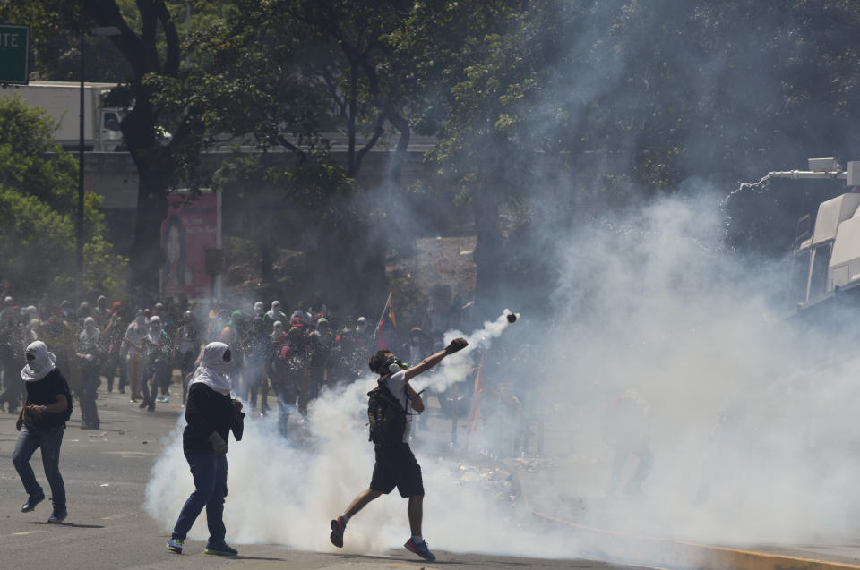 An anti-government demonstrator wearing a mask, throws a tear gas canister fired by Bolivarian National Police towards a water cannon vehicle, during clashes in a protest at the Central University of Venezuela, UCV, in Caracas, Venezuela, Thursday, March 20, 2014. Thursday dawned with two more opposition politicians, San Cristobal Mayor Daniel Ceballos and San Diego Mayor Enzo Scarano, behind bars. Police used tear gas and water cannons to disperse a student-called protest of several thousand people in Caracas, some of those demonstrating against the arrests of the mayors. (AP Photo/Esteban Felix