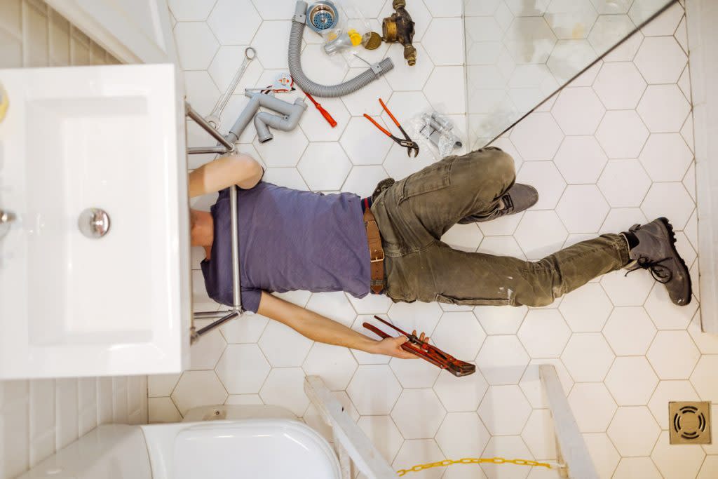 A man fixes a pipe underneath his sink. 