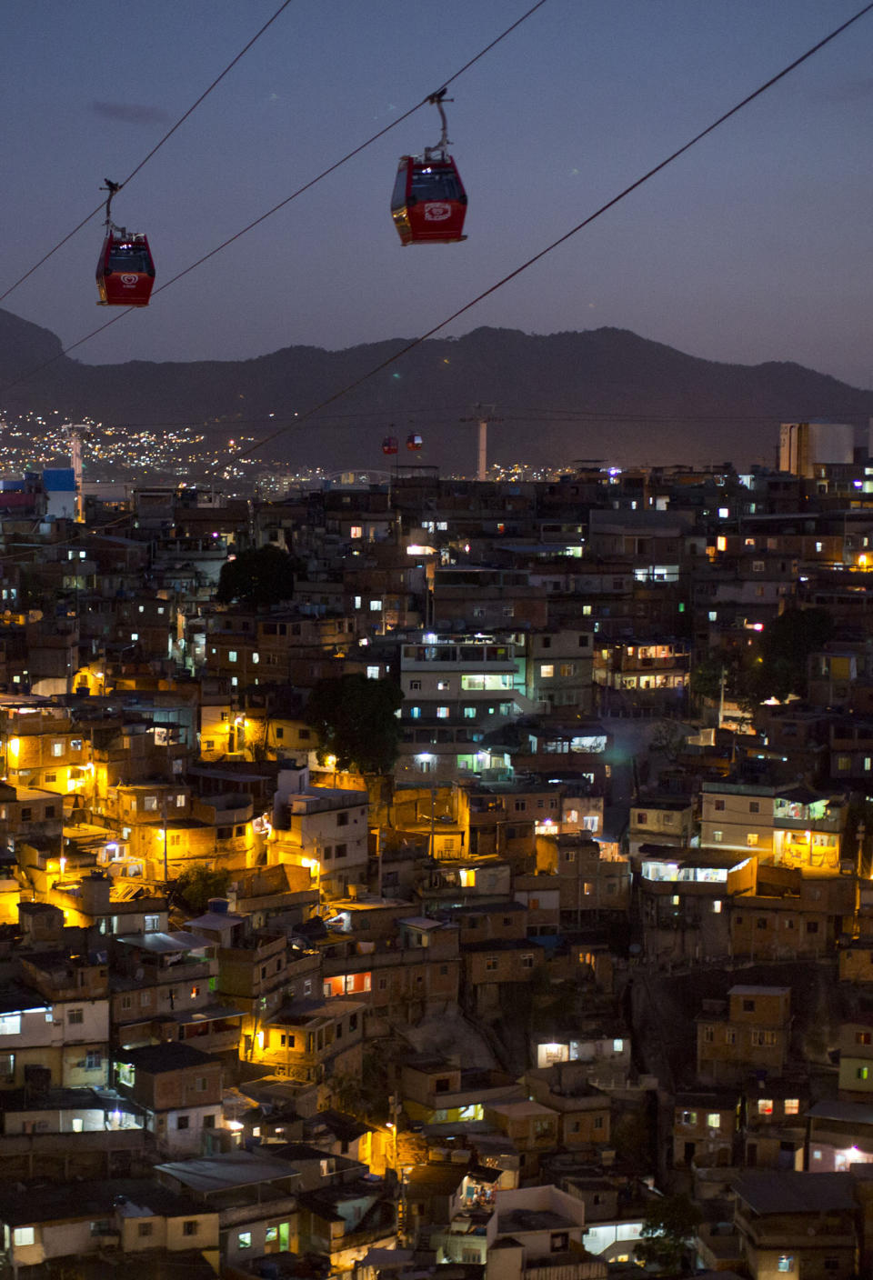 In this May 10, 2013 photo, homes are lit at night as cable-cars move commuters over the Complexo do Alemao complex of shantytowns in Rio de Janeiro, Brazil. The cable-car system linking six of its hilltops over a 3.5-kilometer (2.3-mile) route has become a popular tourist attraction. (AP Photo/Felipe Dana)