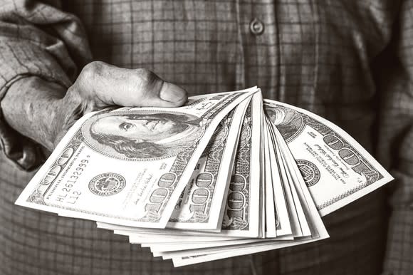 A man holding a fanned stack of hundred dollar bills.