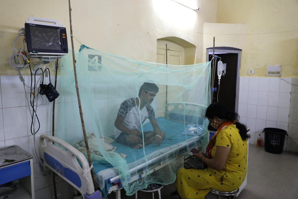 A woman sits with a dengue patient protected by a mosquito net at a government hospital in Prayagraj, in India's Uttar Pradesh state on September 15, 2021.