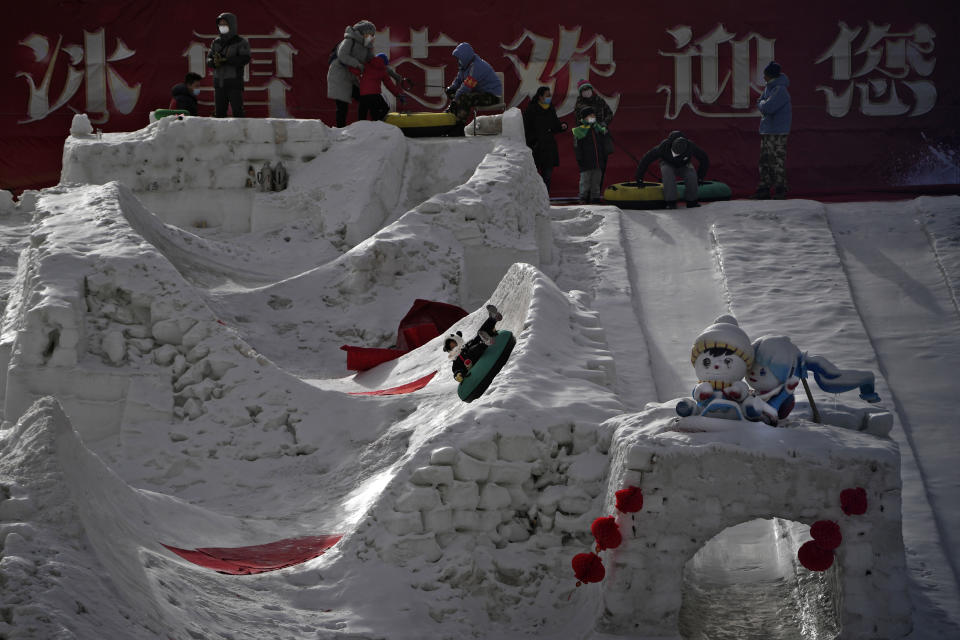 Residents bring their children to enjoy a slide in the snow at a public park in Beijing, Thursday, Jan. 19, 2023. China on Thursday accused "some Western media" of bias, smears and political manipulation in their coverage of China's abrupt ending of its strict "zero-COVID" policy, as it issued a vigorous defense of actions taken to prepare for the change of strategy. (AP Photo/Andy Wong)