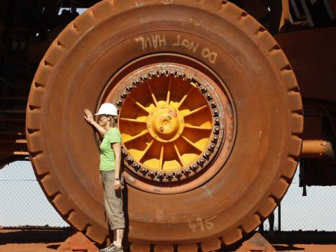 A tourist stands beside a wheel of a parked tipper truck at an iron ore mine