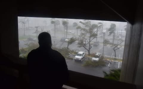 A man looks on as trees fall onto cars in Puerto Rico - Credit: HECTOR RETAMAL/AFP