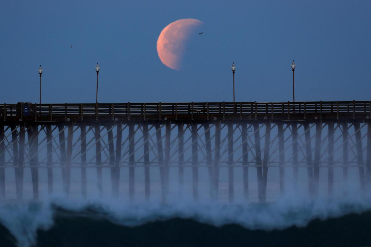 A blue moon comes out of a lunar eclipse as it sets past an ocean pier in Oceanside, California: Reuters