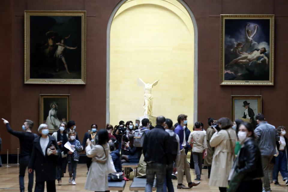 People stroll in the Louvre museum with the marble hellenic sculpture The Winged Victory of Samothrace, in the background, Wednesday, May, 19, 2021 in Paris. Museums must restrict entries so there is 8 square meters of space (86 square feet) per visitor. Café and restaurant terraces are reopening Wednesday after a shutdown of more than six months deprived people of what feels like the essence of life — sipping coffee and wine with friends outdoors — to save lives during the coronavirus pandemic. (AP Photo/Thibault Camus)