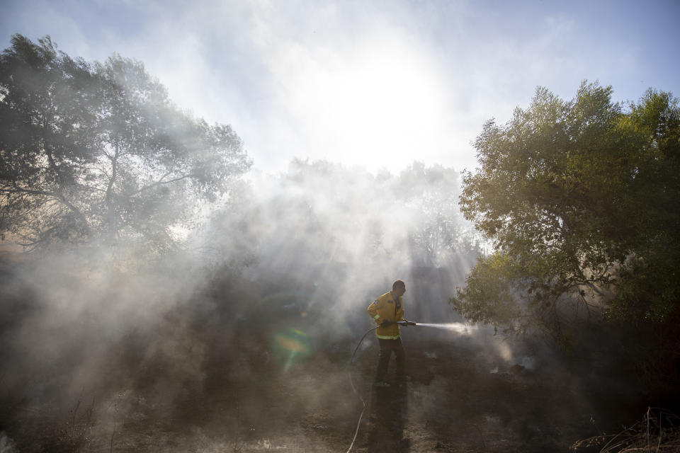 A firefighters attempts to extinguish a fire started by an incendiary device launched from the Gaza Strip, in Kibbutz Kfar Aza on the border with Gaza, Monday, Aug. 24, 2020. Militants affiliated with Hamas have launched scores of incendiary balloons into southern Israel in recent weeks in a bid to pressure Israel to ease the blockade imposed since Hamas took control of the territory in 2007. (AP Photo/Ariel Schalit)