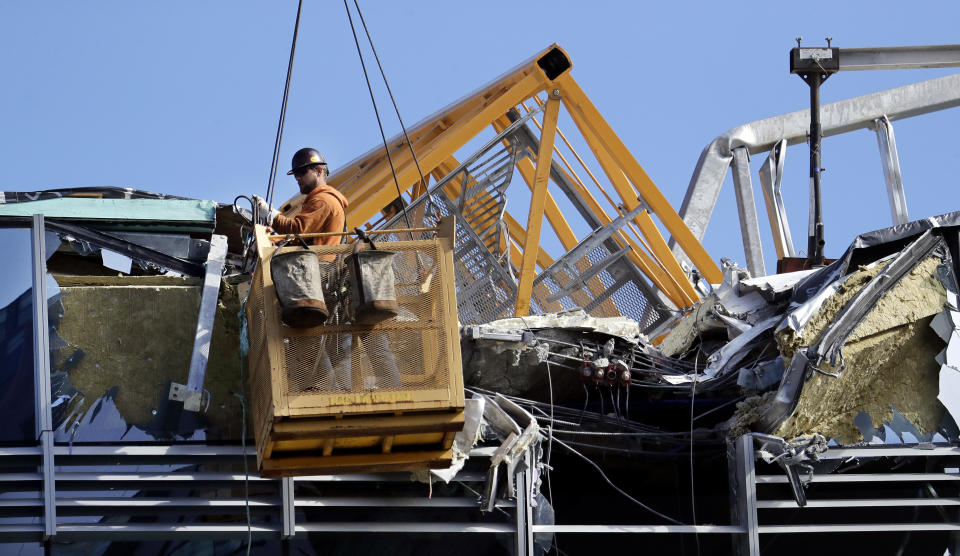 With a portion of the broken crane on the roof behind, a worker suspended in a basket clears debris from a building damaged when the crane atop it collapsed a day earlier, Sunday, April 28, 2019, in Seattle. The construction crane fell from a building on Google's new campus during a storm that brought wind gusts, crashing down onto one of the city's busiest streets and killing multiple people. (AP Photo/Elaine Thompson)