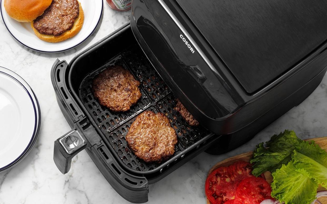 Easy Grilled Hamburgers; How to; marble surface; overhead camera angle; step #5; burger patties in air fryer basket not touching; veggie tray; lettuce; onions; tomato; tomato slices; hamburger; burger; white plates; ketchup; ketchup bottle; prep; in process