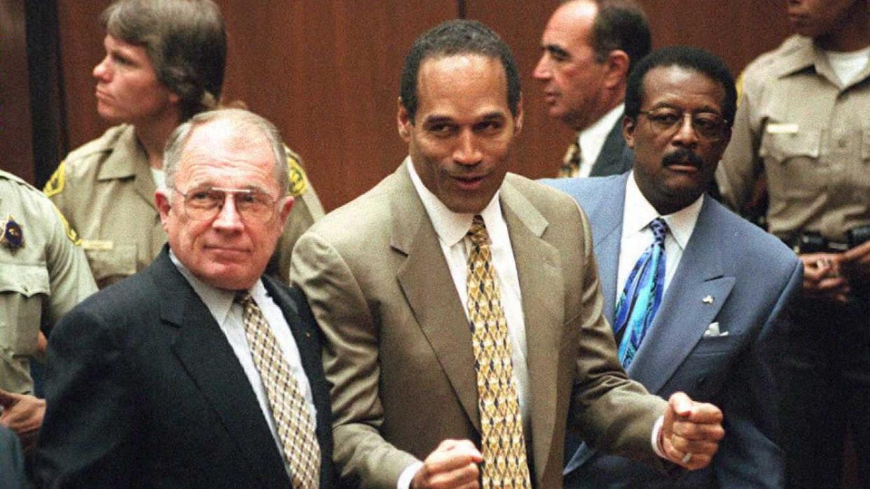 f lee bailey stands and looks left, oj simpson holds his fists in front of him and looks left, johnnie cochran stands and looks left, all three men wear suits with ties