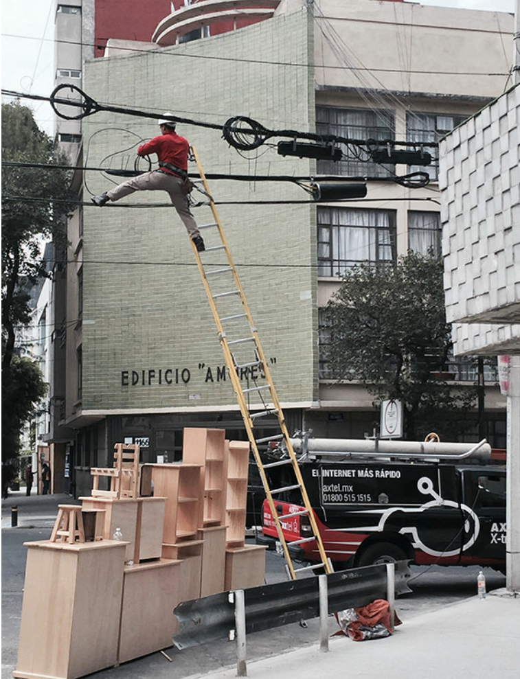 A worker has used a ladder to reach phone cables high above the street; the ladder is only leaned against the flimsy cords, not a wall, so could easily collapse