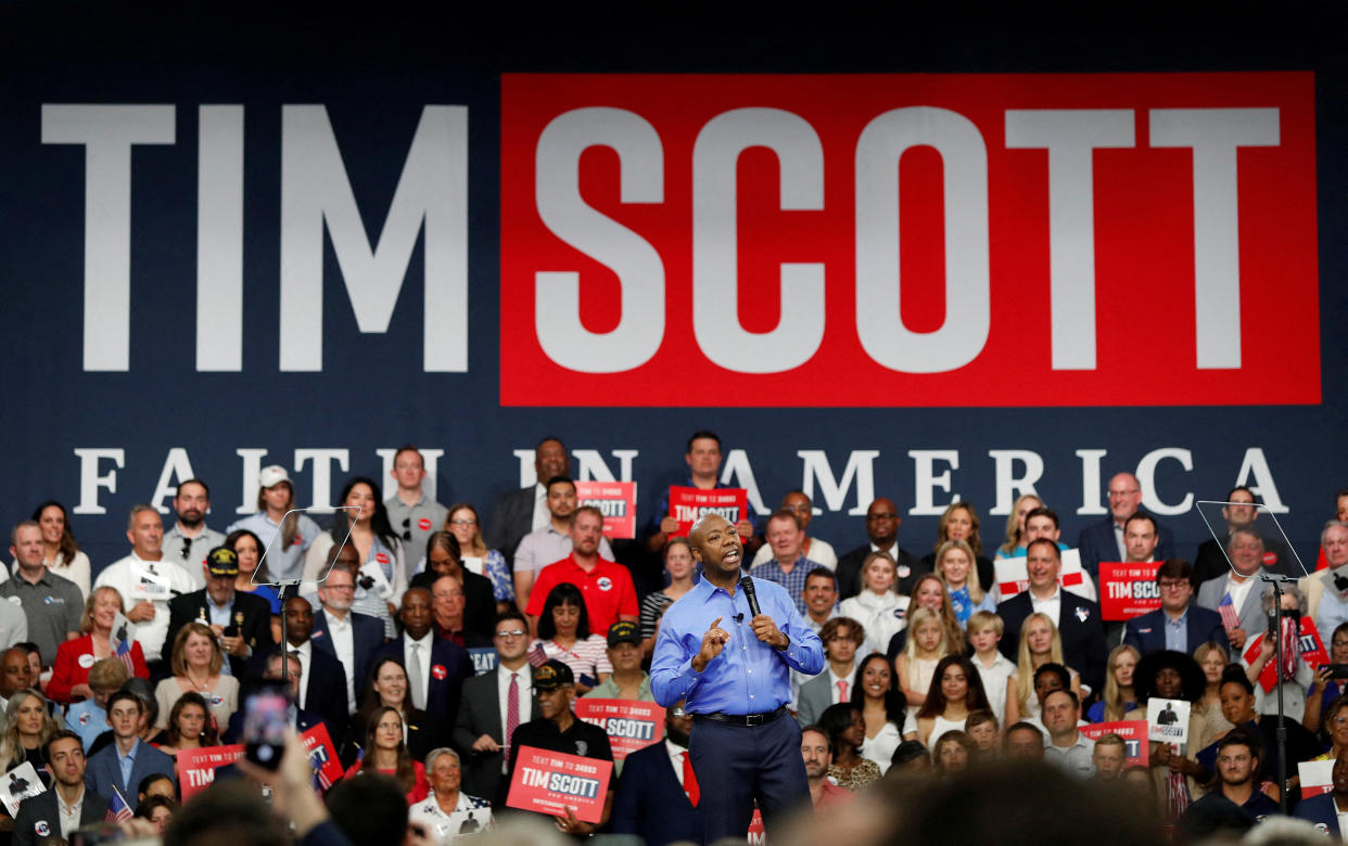 Sen. Tim Scott gives a speech in front of reporters and a sign saying: Tim Scott, Faith in America.