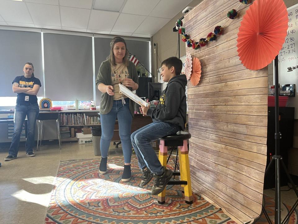 Emily Oley, fourth grade teacher at Eyler Elementary School, assists a student as he reads a page from "On the Road to Kindness," a book published by students in the class, during a classroom publishing party.