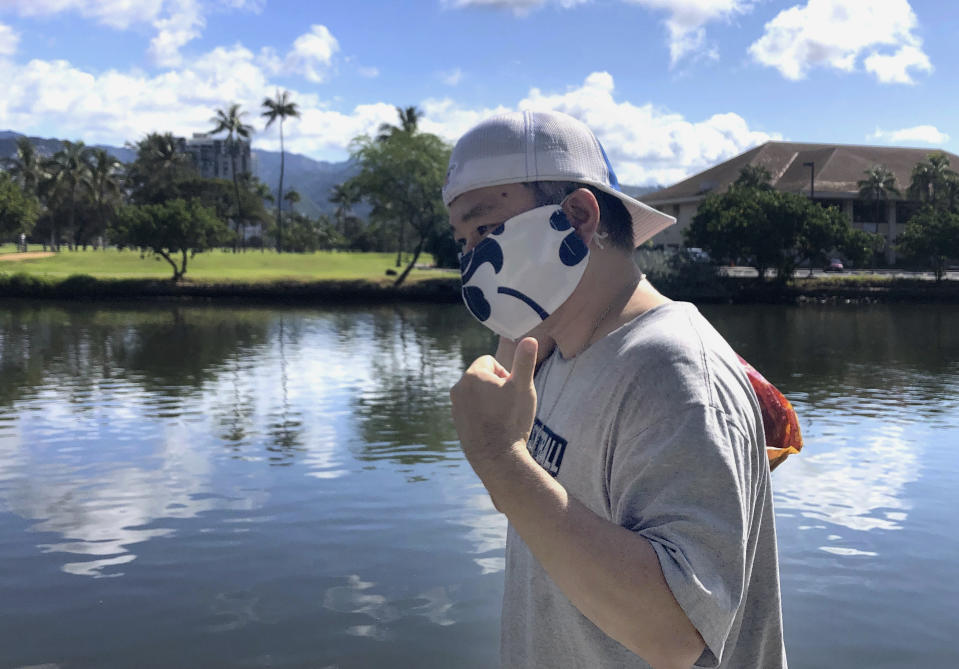 FILE - Ricardo Lay, 52, wearing an aloha print mask, poses for a photo as he walks in the Waikiki neighborhood of Honolulu on April 7, 2020. Hawaii will lift the nation's last statewide indoor mask mandate by March 26, 2022. Hawaii Gov. David Ige says COVID-19 rates in Hawaii are dropping and he expects the trend to continue in the coming weeks. (AP Photo/Caleb Jones, File)