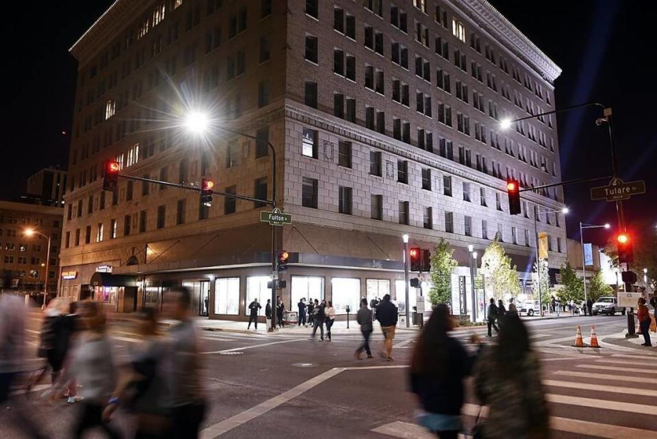 Pedestrians cross Tulare Street in front of the illuminated T.W. Patterson Building in downtown Fresno following the grand reopening of Fulton Street on Oct. 21, 2017.