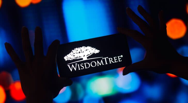 Hands holding a smartphone showing the WisdomTree logo in front of a digital blue and orange background.