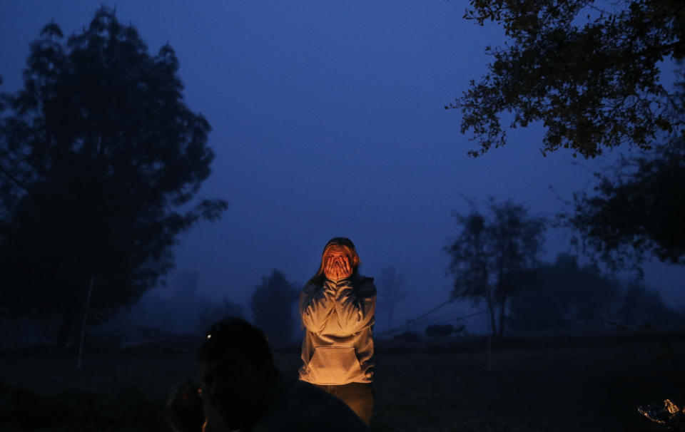 In this Nov. 14, 2018, photo, Arissa Harvey holds her hands up to her face while staying warm beside a fire in Paradise, Calif. Harvey's family lost their home in the Camp Fire and were living in an RV on the property. For a while, Phillip and Krystin Harvey, who lost their mobile home, had been staying with Arissa and their two other teenage daughters in the camper, trying to hang on to a piece of the life they had known. Eventually the family gave up and moved to Oroville, Calif., to stay with friends to have some stability and security, their cousins Patrick Knuthson said. (AP Photo/John Locher)