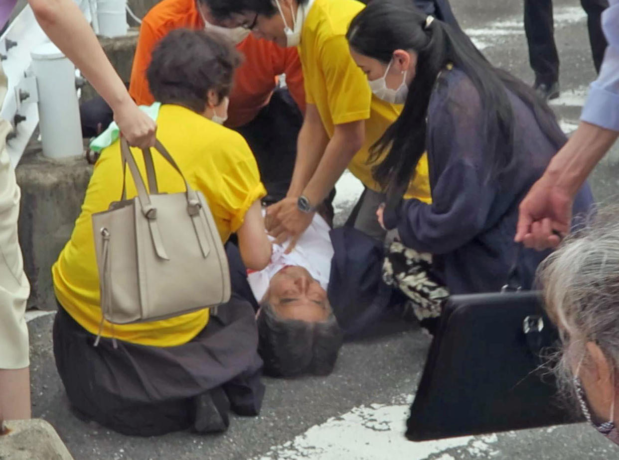 In this image from a video, Japan’s former Prime Minister Shinzo Abe, center, falls on the ground in Nara, western Japan Friday, July 8, 2022. Abe was shot during a campaign speech Friday in western Japan and was airlifted to a hospital but he was not breathing and his heart had stopped, officials said. (Kyodo News via AP)