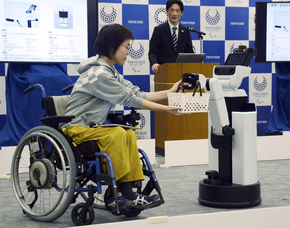 A robot passes a basket containing drinks to a woman in wheelchair during an unveiling event in Tokyo Friday, March 15, 2019. Organizers on Friday showed off robots that will be used at the new National Stadium to provide assistance for fans using wheelchairs. (Kyodo News via AP)