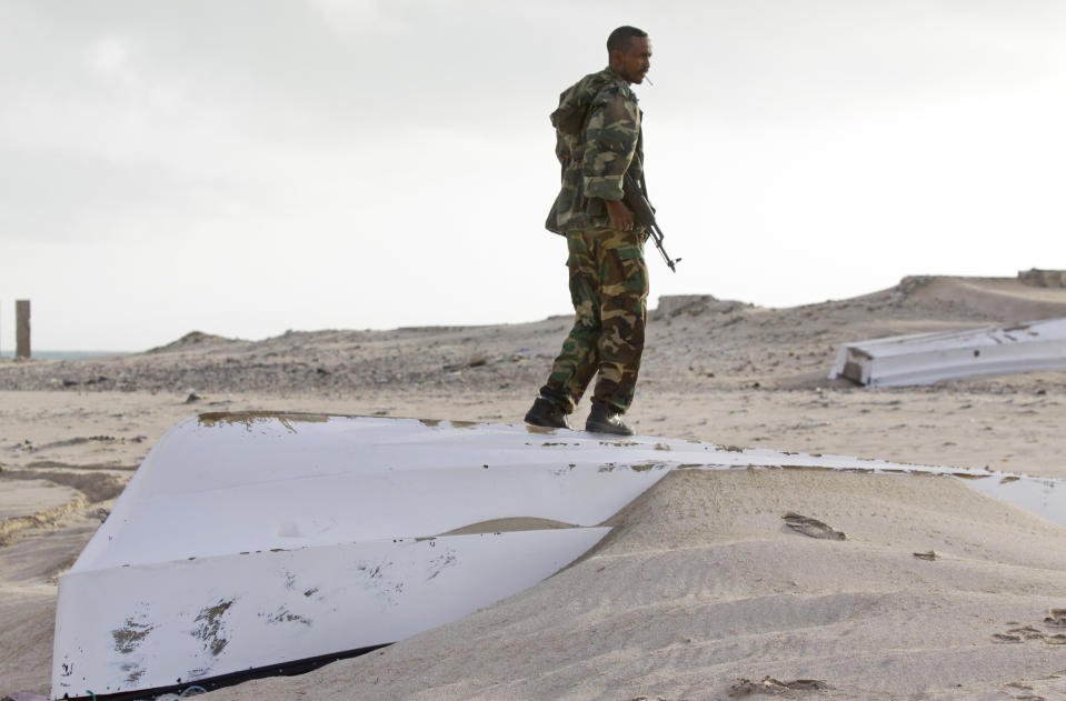 In this photo taken Sunday, Sept. 23, 2012, a Somali government soldier stands over one of the overturned pirate skiffs that litter the dunes on the shoreline near the once-bustling pirate den of Hobyo, Somalia. The empty whisky bottles and overturned, sand-filled skiffs that litter this shoreline are signs that the heyday of Somali piracy may be over - most of the prostitutes are gone, the luxury cars repossessed, and pirates talk more about catching lobsters than seizing cargo ships. (AP Photo/Farah Abdi Warsameh)