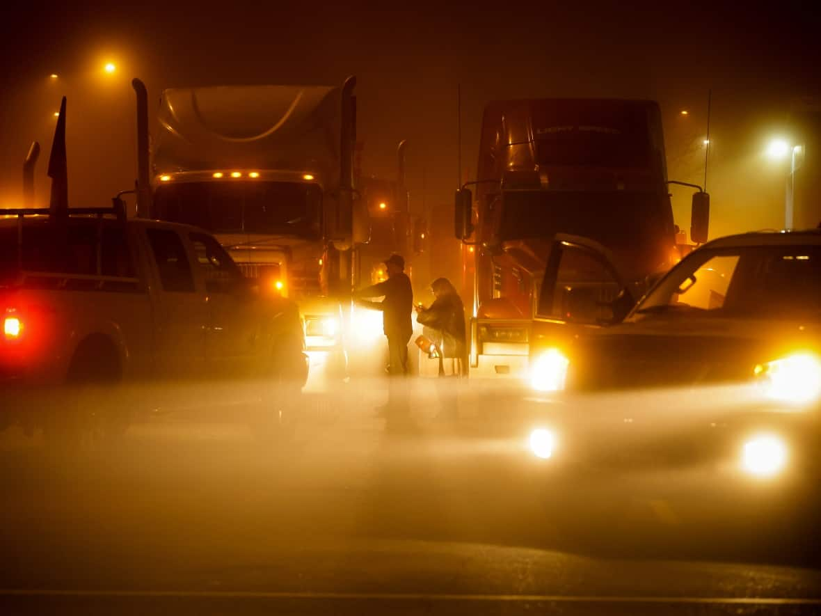 A trucker tapes a sign on the side of his truck before departing with a cross-country convoy destined for Ottawa to protest a federal vaccine mandate for truckers in Delta, B.C. (Darryl Dyck/Canadian Press - image credit)