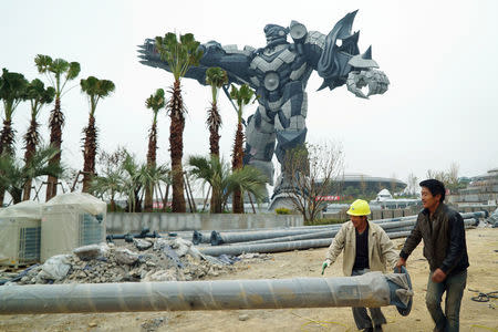 Construction workers carry a light pole in front of a giant robot statue at the Oriental Science Fiction Valley theme park in Guiyang, Guizhou province, China November 16, 2017. REUTERS/Joseph Campbell/Files