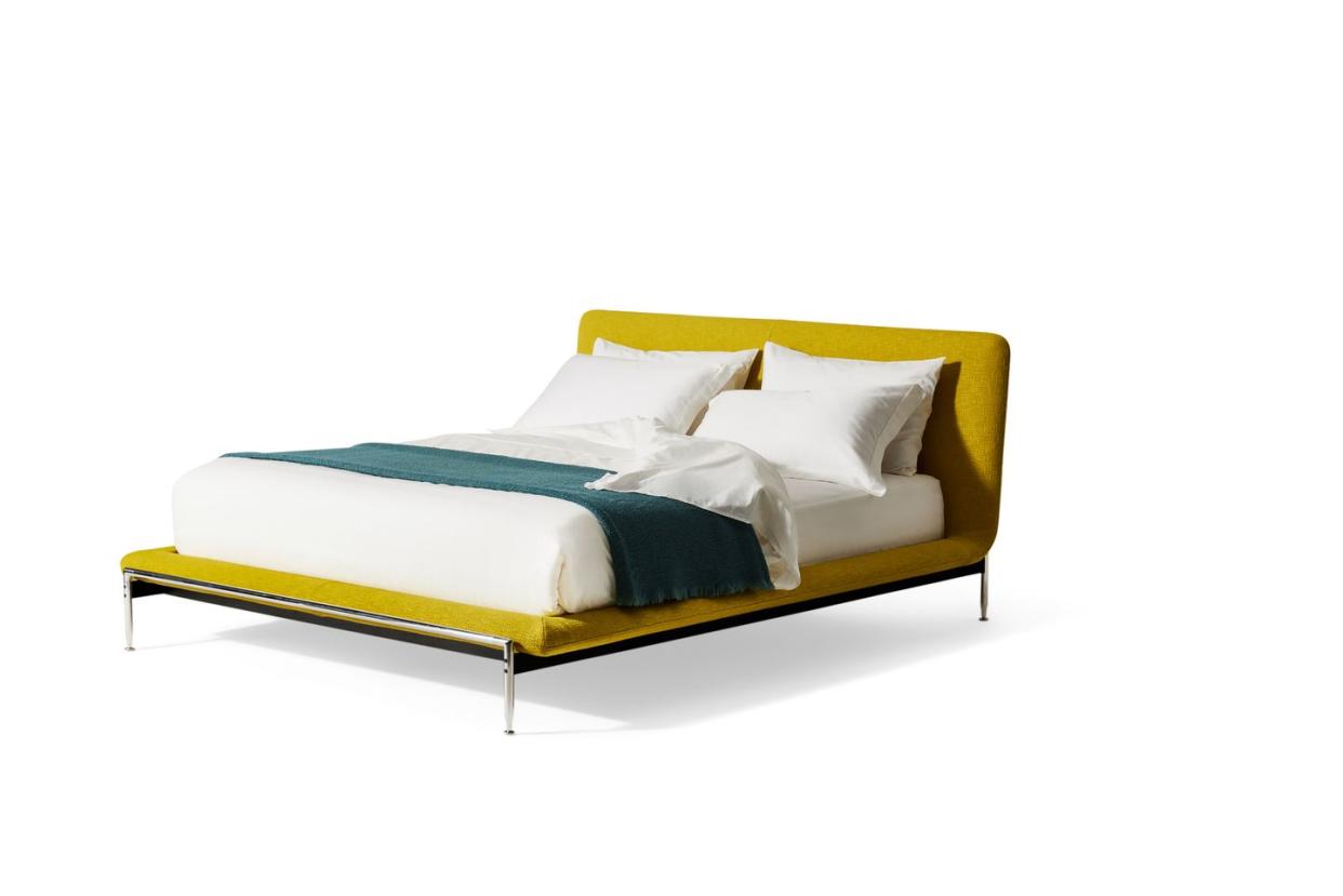 yellow bed on spindly legs with white sheets and green throw on it