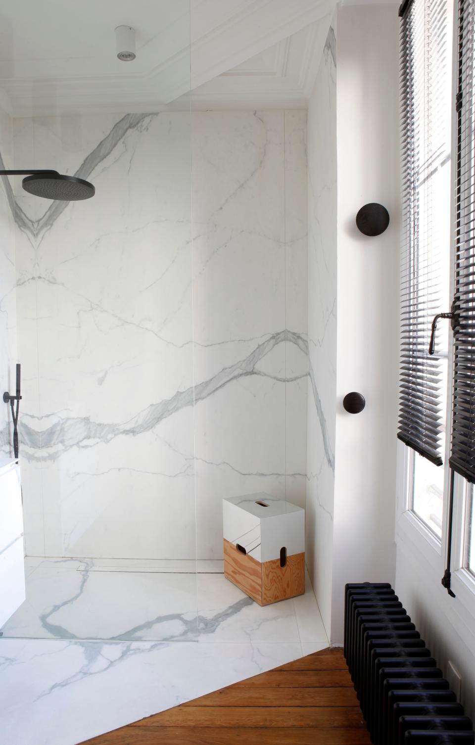 The walls are covered in large tiles printed to look like marble by Ariostea. The fixtures are by Fantini and the stool in the shower is inspired by Le Corbusier.