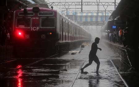 A commuter crosses waterlogged railway tracks as a suburban train is seen parked at a railway station after its services were suspended during heavy monsoon rains in Mumbai