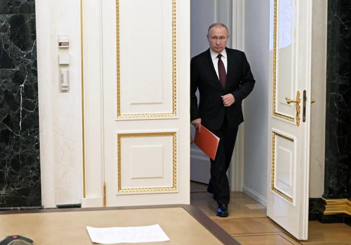 Russian President Vladimir Putin enters a gilt-encrusted open door in the Kremlin carrying a red folder.