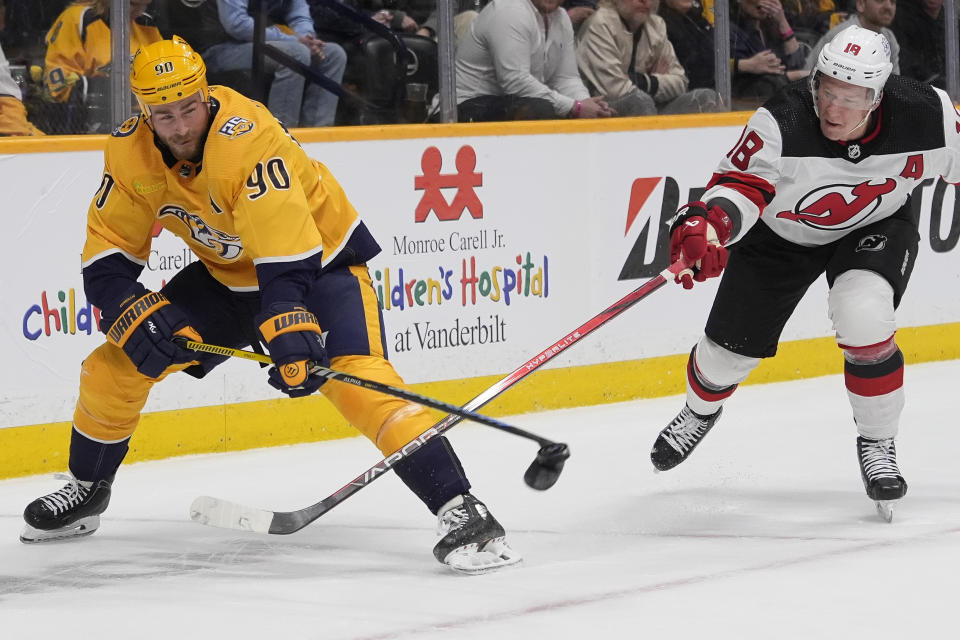 Nashville Predators center Ryan O'Reilly (90) hits the puck away from New Jersey Devils left wing Ondrej Palat (18) during the first period of an NHL hockey game Tuesday, Feb. 13, 2024, in Nashville, Tenn. (AP Photo/George Walker IV)