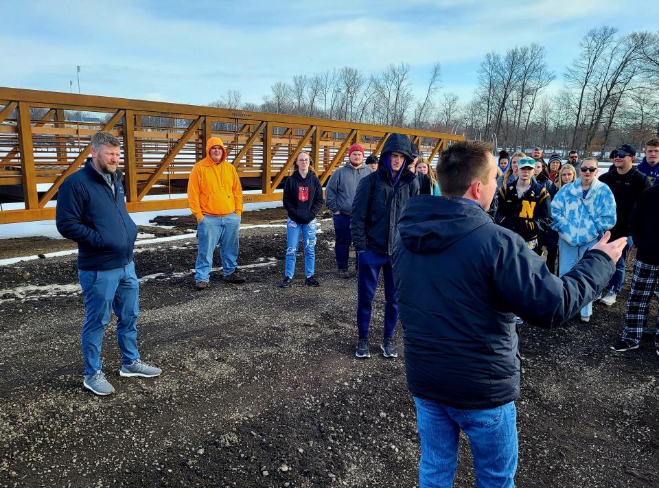 Port Huron Engineering Manager Brent Moore, right, breaks down the planning process for the Black River Canal bridge and pedestrian path — the bridge structure waiting placement behind them — to local high school students on Thursday, March 16, 2023, while teacher Kyle Whymer, left, watches on.
