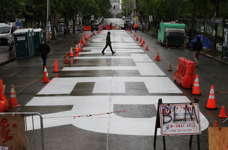 A man walks across the street over freshly painted sign that reads 'Black Lives Matter' near Seattle Police Department East Precinct in Seattle