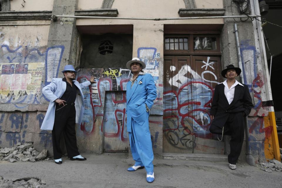 Guardarrama Tapia, Jesus Gonzalez de la Rosa and Flores Mujica wears their Pachuco outfits while posing for a photograph next to a wall with graffiti in Mexico City
