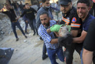 Palestinians carry the body of a child found in the rubble of a house belonging to the Al-Tanani family, that was destroyed in Israeli airstrikes in town of Beit Lahiya, northern Gaza Strip, Thursday, May 13, 2021. (AP Photo/Abdel Kareem Hana)