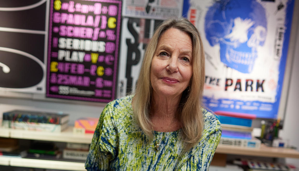  Image of Paula Scher in front of posters of her work. 