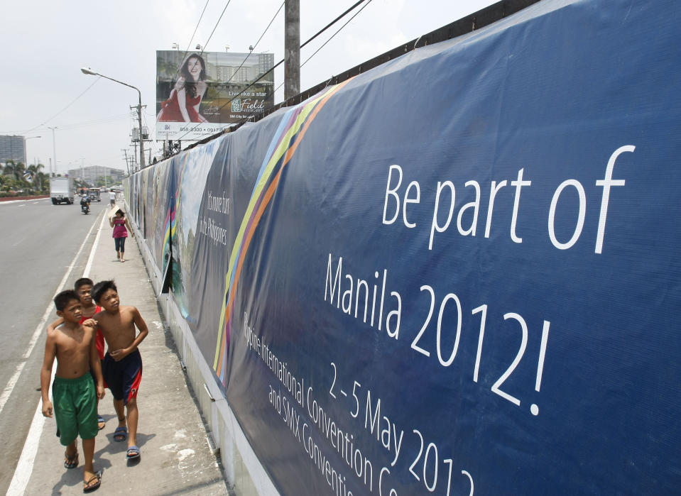 Boys walk past a wall covered with a tarpaulin poster of the ongoing 45th Annual Board of Governors meeting of the Asian Development Bank at suburban Pasay city south of Manila, Philippines, Thursday May 3, 2012. Delegates attending the international conference of the ADB in the Philippines capital may not see what they came to discuss: abject poverty. The makeshift, temporary wall on both sides of the bridge from the airport to downtown Manila, hides a sprawling slum along a garbage-strewn creek. (AP Photo/Bullit Marquez)