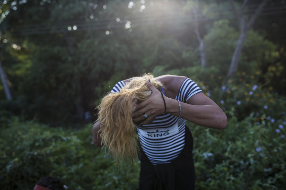 In this Nov. 2, 2018 photo, Honduran transgender Teresa Perez, who part of about 50 LGBTQ migrants traveling with the Central American migrants caravan hoping to reach the U.S. border, gathers her hair into a ponytail, on the outskirts of Donaji, Mexico. Sticking out among the crowd for their bright clothing and makeup, the group has suffered verbal harassment, especially from men. (AP Photo/Rodrigo Abd)