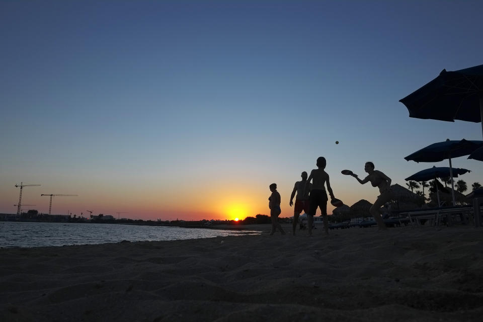 People play beach racket at the beach during sunset in coastal resort of Ayia Napa in the eastern Mediterranean island of Cyprus, Saturday, Aug. 22, 2020. Health Minister Constantinos Ioannou has extended until Jan. 15, 2021, a ban on outdoor festivals, concerts and exhibitions in places without seating where social distancing rules can't be enforced. (AP Photo/Petros Karadjias)