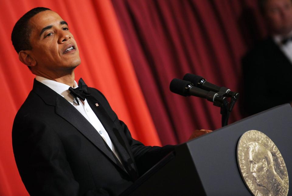 barack obama, wearing a red tuxedo, speaking at a podium with the nobel peace prize logo in front of it